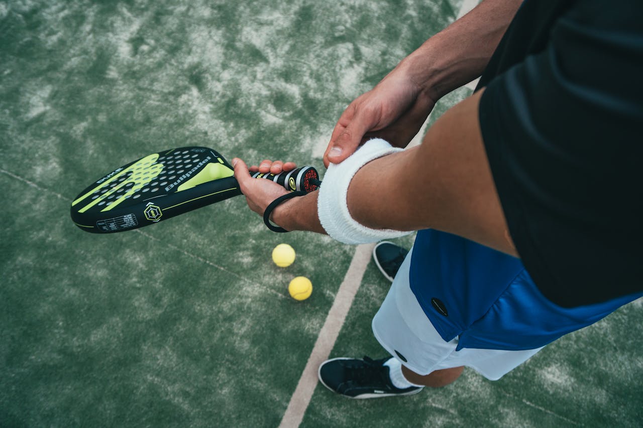 creative-01 Close-up of a male padel player adjusting wristband on a court. Sports action focused.