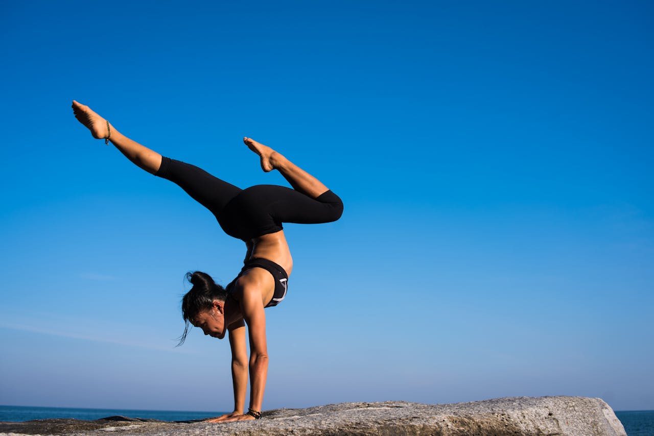 brand-03 A woman performing a yoga handstand on a rock by the sea under a clear blue sky.