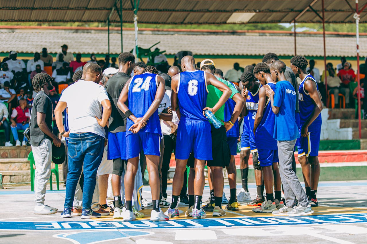 creative-03 A basketball team strategizes in a huddle during an outdoor game with spectators.