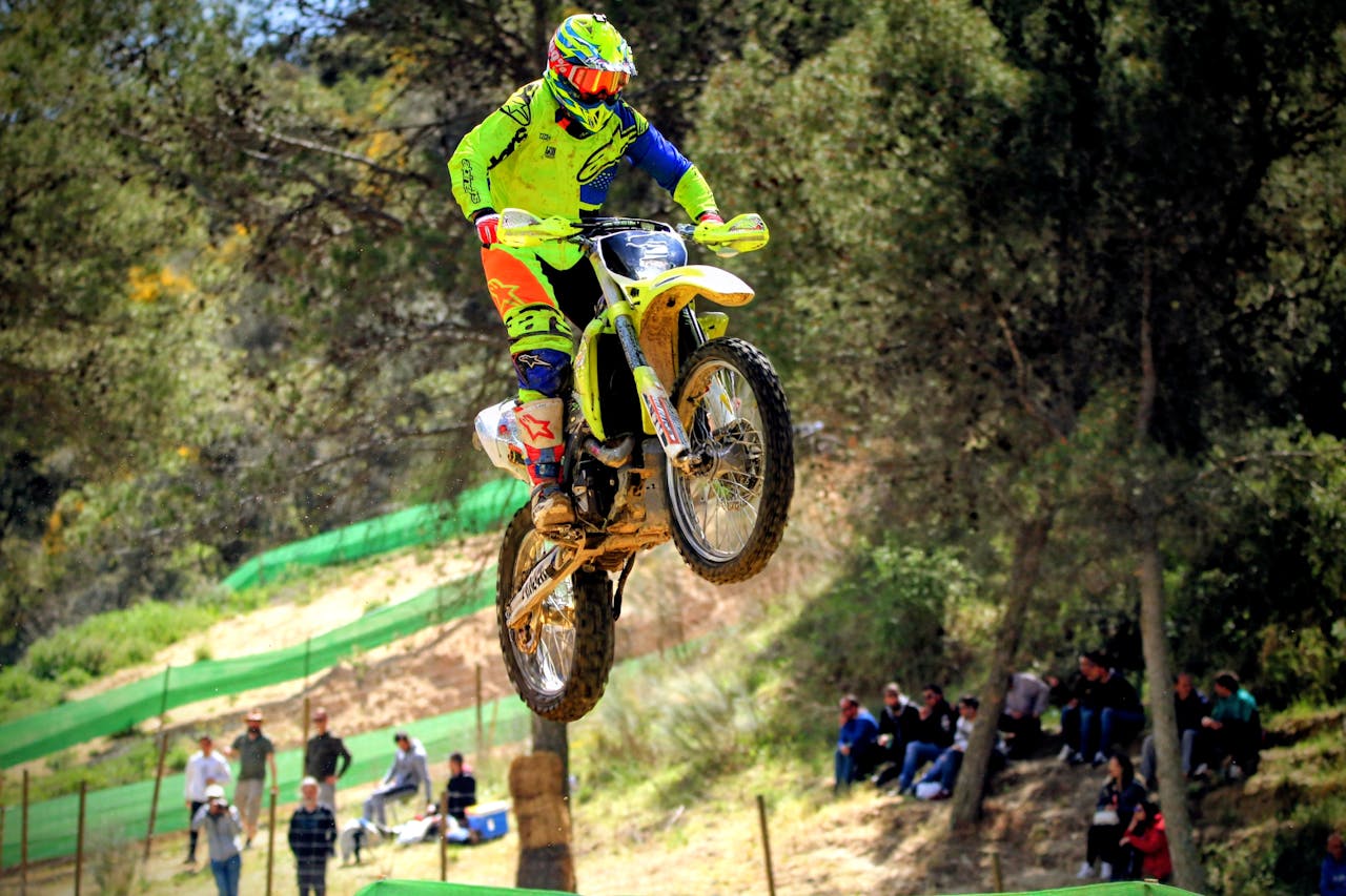 mobile-01 Dynamic action shot of a motocross rider in vibrant gear catching air during a forest race.