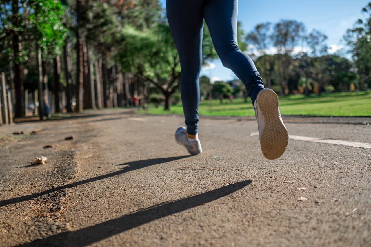creative-02 A woman running outdoors on a sunny day along a scenic park trail, focusing on fitness and health.